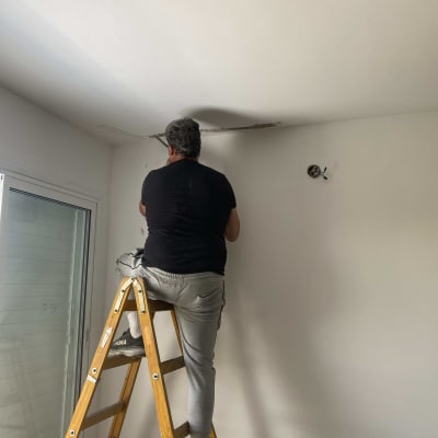 חשמלאי עובד על תקרה בעזרת סולם וכלים