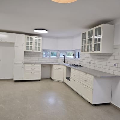 מטבח נקי עם ארונות לבנים ומשטח עבודה אפור