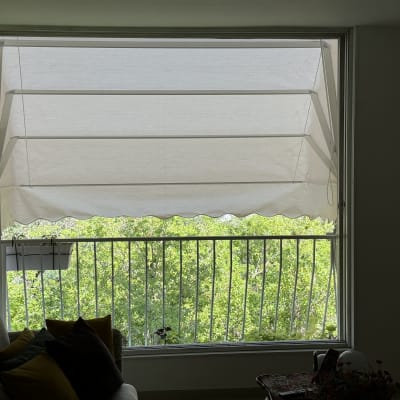 סוכך בד לבן על חלון גדול עם נוף ירוק