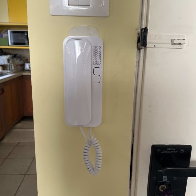 אינטרקום לבן תלוי על קיר צהוב עם כבל ספירלי