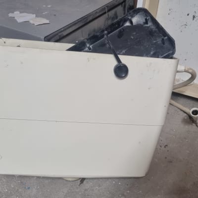 מיכל הדחה ישן עם צינור פלסטיק על רצפה