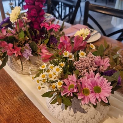 סידור פרחים צבעוני באגרטל לבן על שולחן עץ