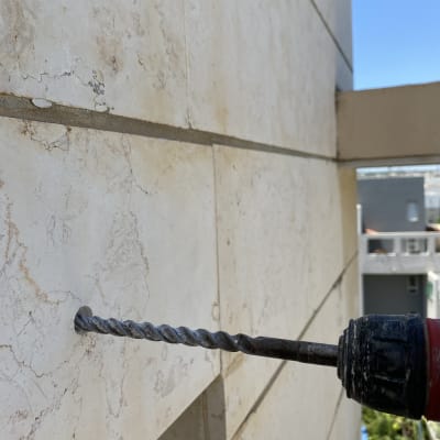 מקדחה חשמלית קודחת בקיר חיצוני של בניין