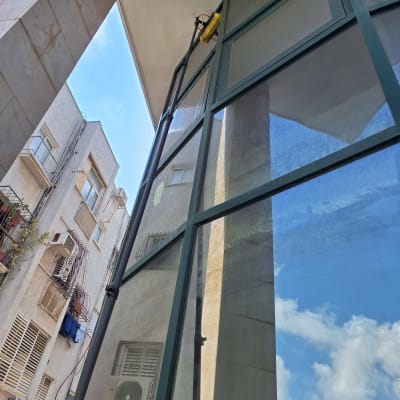 אדם מנקה חלון גבוה עם מברשת על מוט ארוך