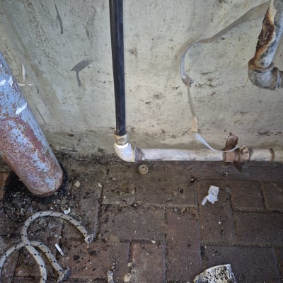 צינור מתכת חלוד עם חיבורי פלסטיק על קיר בטון