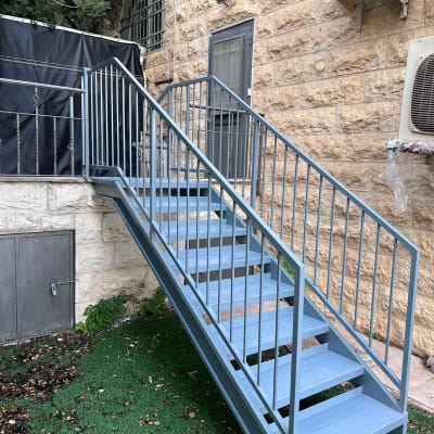 מדרגות מתכת עם מעקה ליד קיר אבן