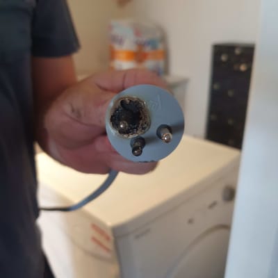 תקע חשמלי שרוף מוחזק ביד של חשמלאי