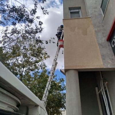 אדם על סולם מבצע עבודות בגובה על בניין