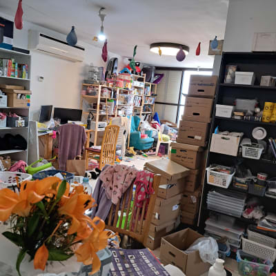 חדר מבולגן עם קופסאות קרטון ומדפים מלאים בחפצים.