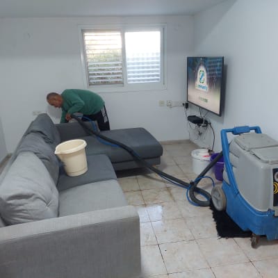 אדם מנקה ספה עם מכונת ניקוי מקצועית