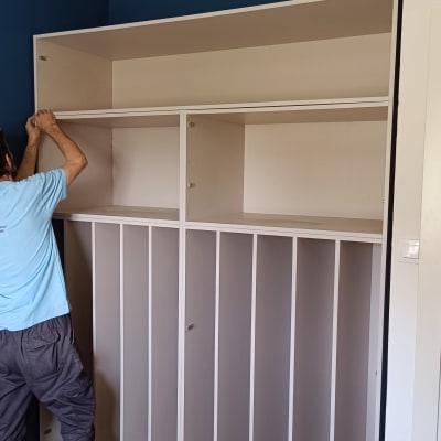 אדם מתקין ארון עץ בחדר עם קיר כחול