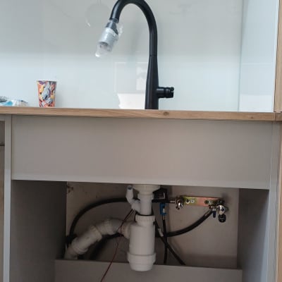 כיור עם ברז וכלי עבודה מתחת לארון מטבח