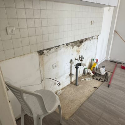 שיפוץ מטבח עם צנרת חשופה וכיסא פלסטיק לבן