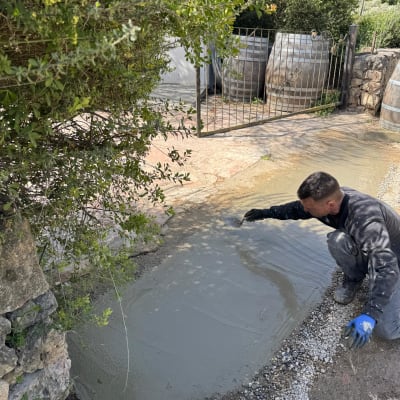 אדם מורח בטון על הקרקע ליד שיחים