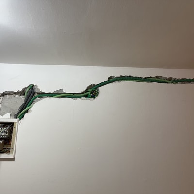 תיבת חשמל פתוחה עם חוטים ירוקים בקיר