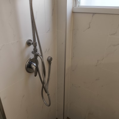 ראש מקלחת עם צינור מתכת על קיר אריחים