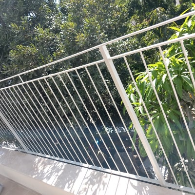 מעקה מתכת לבן עם צמחייה ברקע