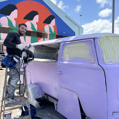 אדם צובע רכב בצבע סגול עם אקדח צבע