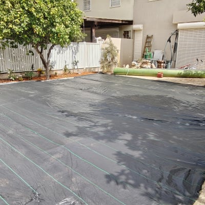 חצר עם יריעות פלסטיק שחורות ועצים מסביב