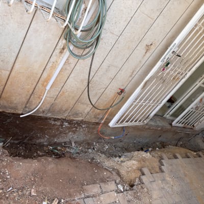 חפירה ליד קיר חיצוני עם צינורות ודלת ברזל