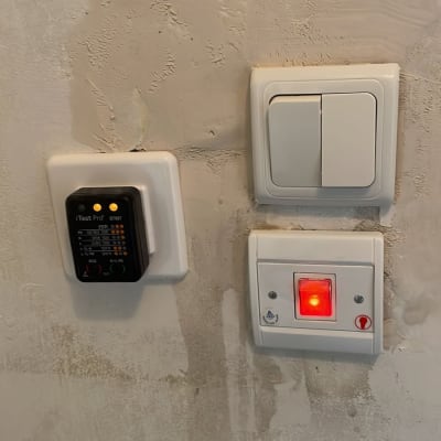 בודק חשמל מחובר לשקע קיר עם מתגי חשמל