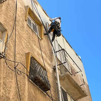 עובד בגובה בגלישת חבלים מבצע תיקון צינור בחזית בניין