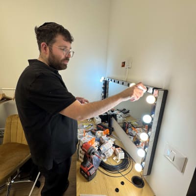 חשמלאי מתקין נורות על מראת איפור עם כלי עבודה