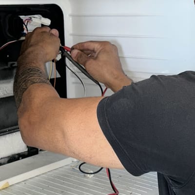 אדם מתקן חוטים במקרר עם מאוורר ירוק