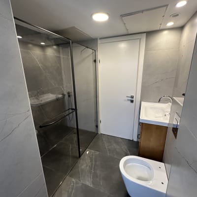 חדר אמבטיה עם מקלחון, כיור ואסלה על רצפה נקייה.