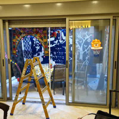 סולם עץ ניצב מול תריס גלילה וחלונות הזזה בפתח מרפסת במהלך עבודות תיקון