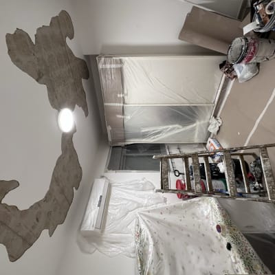 חדר עם קיר מתקלף, סולם, פחיות צבע וציוד צביעה