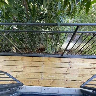 מרפסת עץ עם מעקה מתכת ועצים ברקע