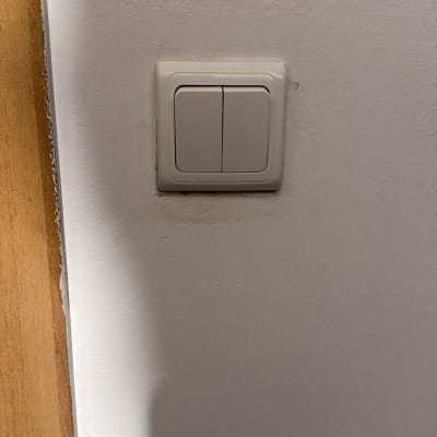 מתג חשמלי על קיר לבן ליד דלת עץ