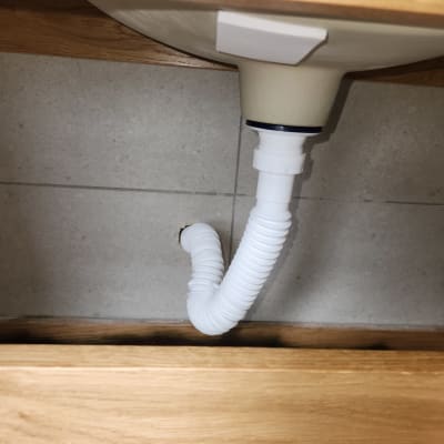 כיור עם צינור פלסטיק מתחת לארון עץ