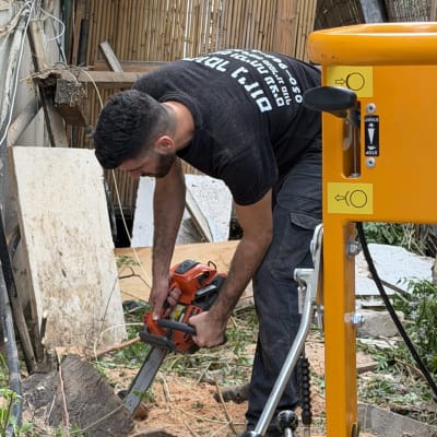 אדם משתמש במסור חשמלי לחיתוך עץ בגינה