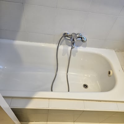 אמבטיה נקייה עם ברז ומגבת ירוקה על הרצפה