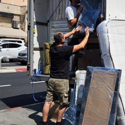 אנשים מעמיסים משאית עם מזרנים וארגזים ברחוב