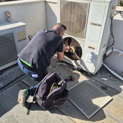 טכנאי עובד על מזגן על גג עם כלים ותיק