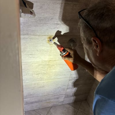 אדם משתמש במבער על קיר אריחים בחדר אמבטיה