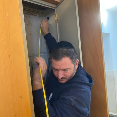 אדם בודק ארון עם כבל צהוב לאיתור נזילות