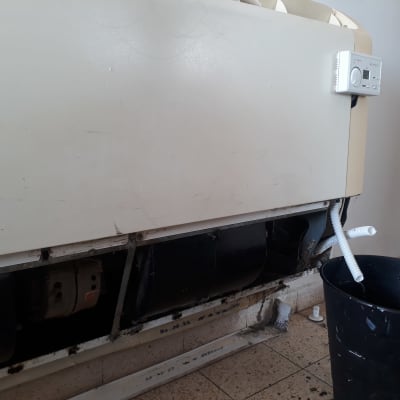 מזגן עם צינור ניקוז ודלי שחור מתחתיו