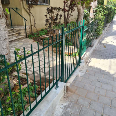 גדר מתכת ירוקה ליד מדרכה ועצים