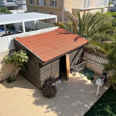 מחסן עץ עם גג רעפים אדום, צינור מים ועגלת קניות