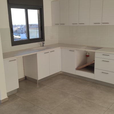 מטבח ריק עם ארונות לבנים ורצפה נקייה