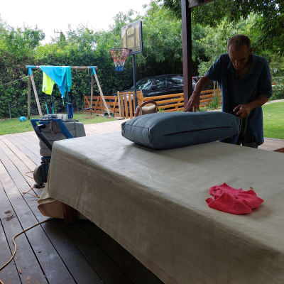 אדם מנקה כרית ספה עם שואב אבק בחצר