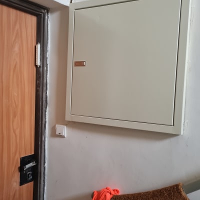 ארון חשמל סגור על קיר לבן ליד דלת עץ