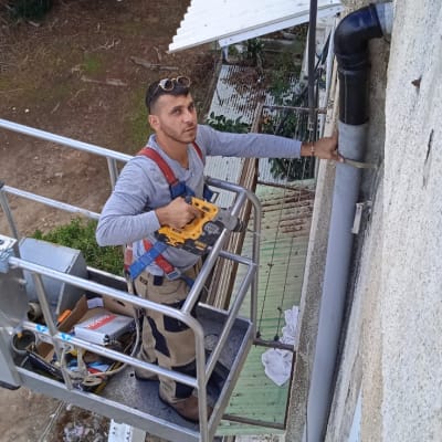 אדם על פיגום ליד גג לבן עם כלי עבודה