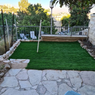 דשא סינתטי מונח על אדמה עם אבנים מסביב