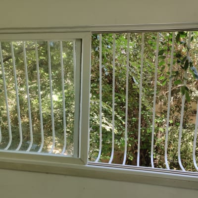 חלון עם סורגים לבנים מול עצים ירוקים