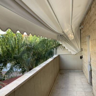 סוכך לבן פרוס מעל מרפסת עם קיר אבן